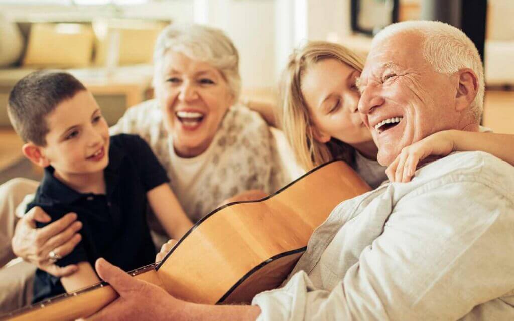 Audífonos al mejor precio | Centros auditivos en tu ciudad 1 Abuelo riendo con su familia mientras toca la guitarra